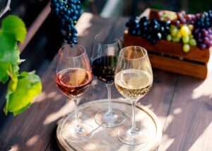 Drei Weingläser mit Weißwein und Roséwein auf Holztisch – Symbol für Vielfalt bei der Weinherstellung - wie wird Wein hergestellt